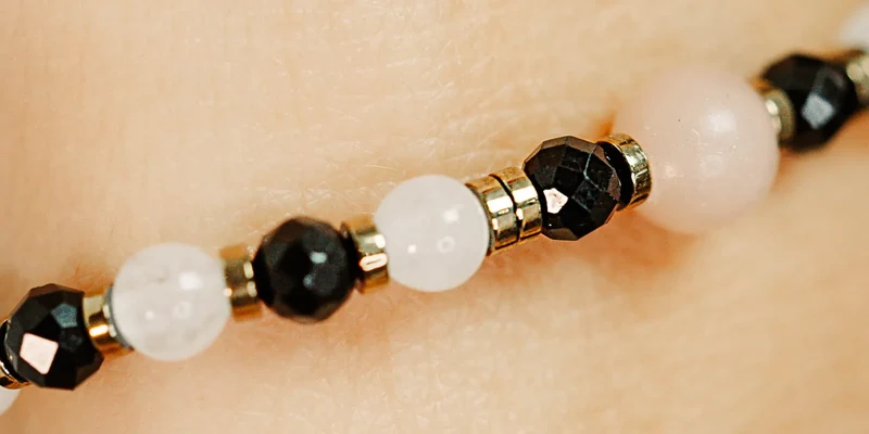 Zbliżenie bransoletki na gumce: jasnoróżowe kulki opalu między czarnymi fasetowanymi kulkami onyksu i złocistymi przekładkami